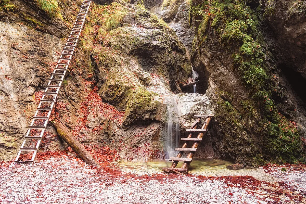 Een metalen ladder naast een watervalletje in een nauwe kloof van het Slowaaks Paradijs, tussen natte rotswanden.