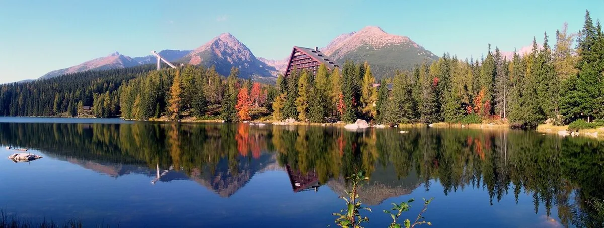 Het bergmeer Štrbské Pleso met donker water, omzoomd door naaldbos, en daarachter de kale toppen van de Hoge Tatra.
